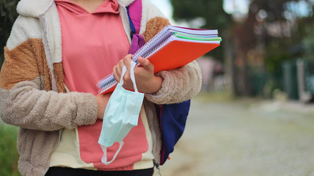 Student holding notebooks and face mask