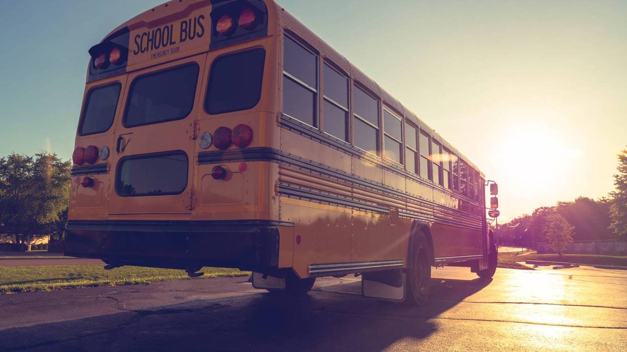 Sunset view of public school transportation with shadow and reflection of dropping sun on road and vehicle moving away