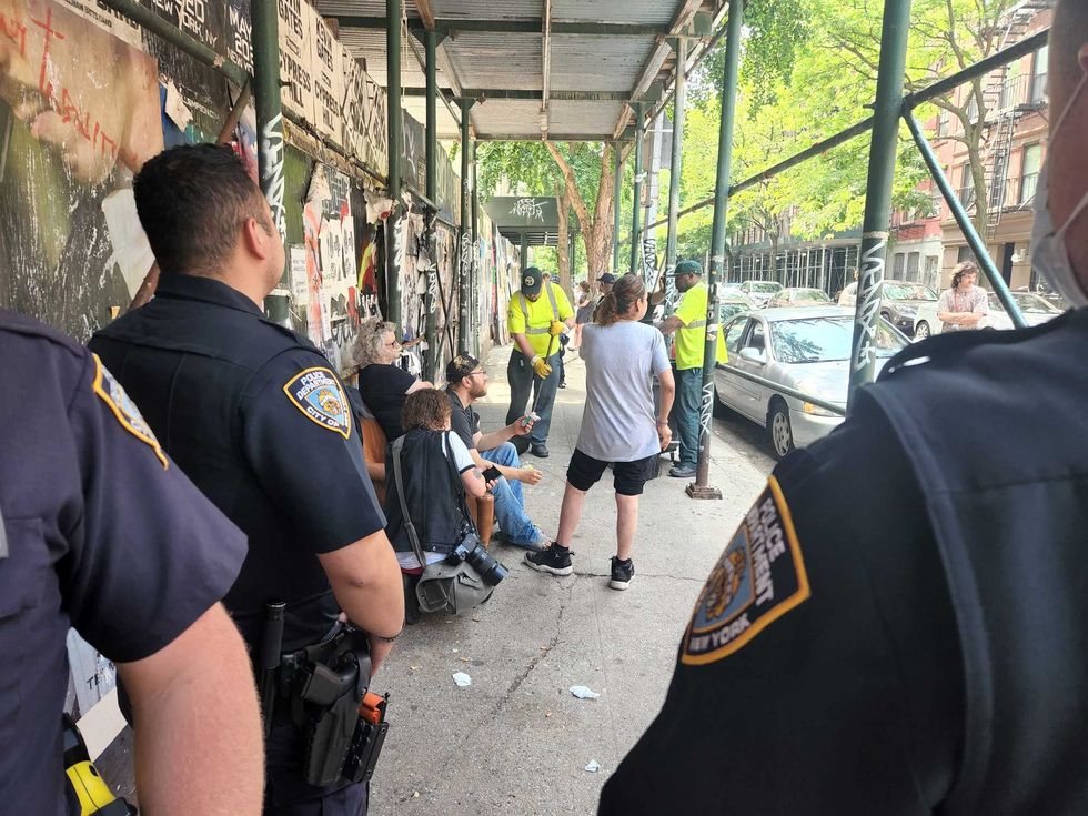 Supportive neighbors stand around a homeless man who refuses to move from his chair as police and sanitation workers try to destroy it during a sweep on June 13, 2022.