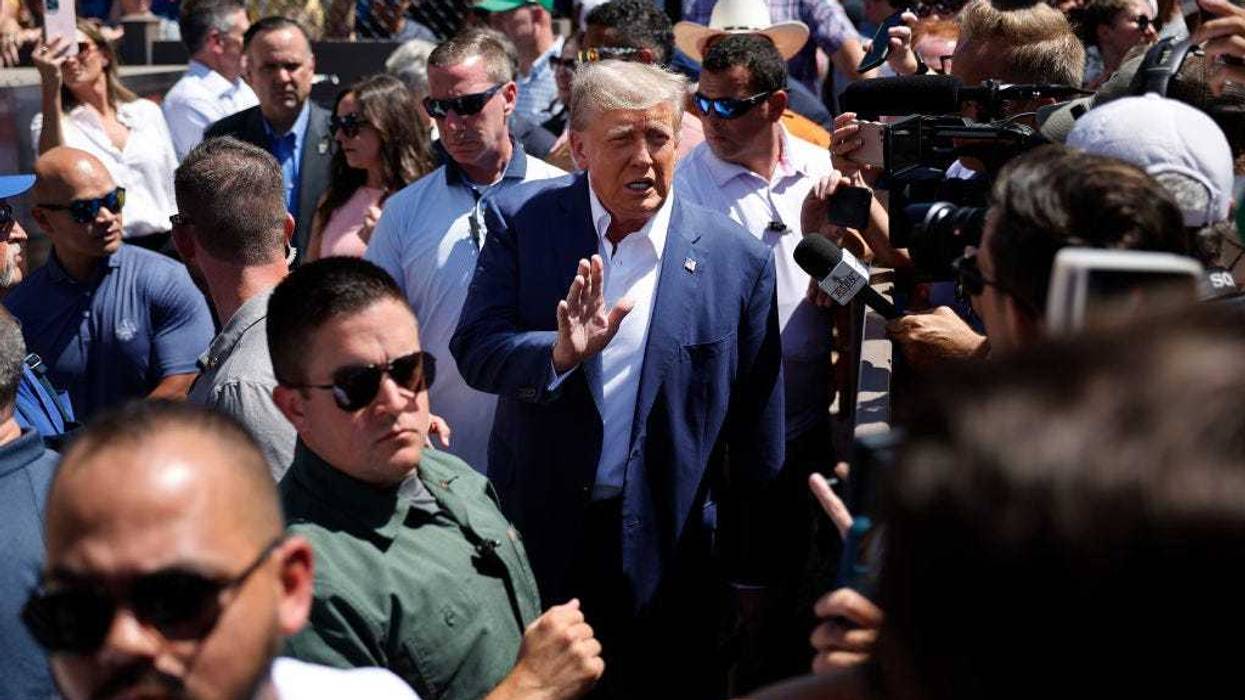 Surrounded by campaign staff and members of the U.S. Secret Service, Former U.S. President Donald Trump (C) waves to supporters as he visits the Iowa Pork Producers Tent at the Iowa State Fair on August 12, 2023 in Des Moines, Iowa.