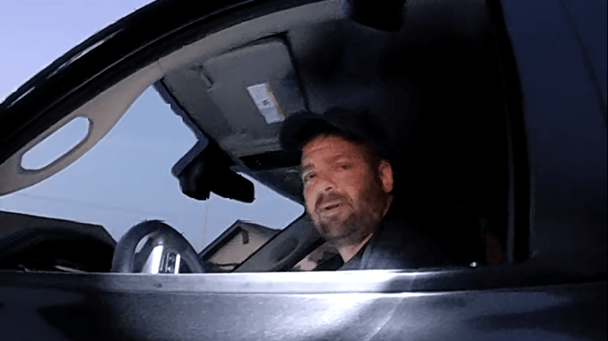 Suspect seen through the driver-side window of his truck. Wearing a dark baseball cap.