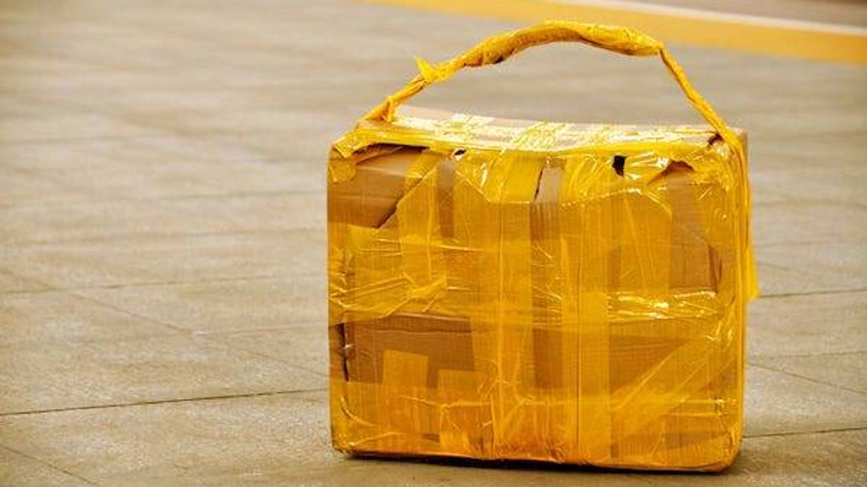 Suspicious looking self made carton suitcase abandoned on sidewalk or platform floor