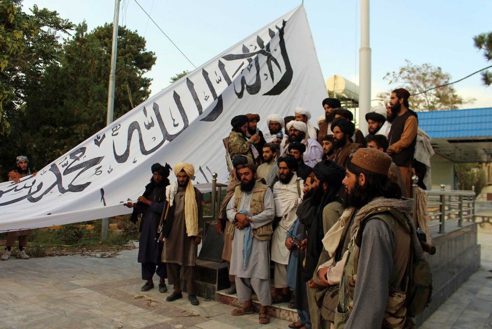 Taliban fighters poses for a photograph while raising their flag Taliban fighters raise their flag at the Ghazni provincial governor