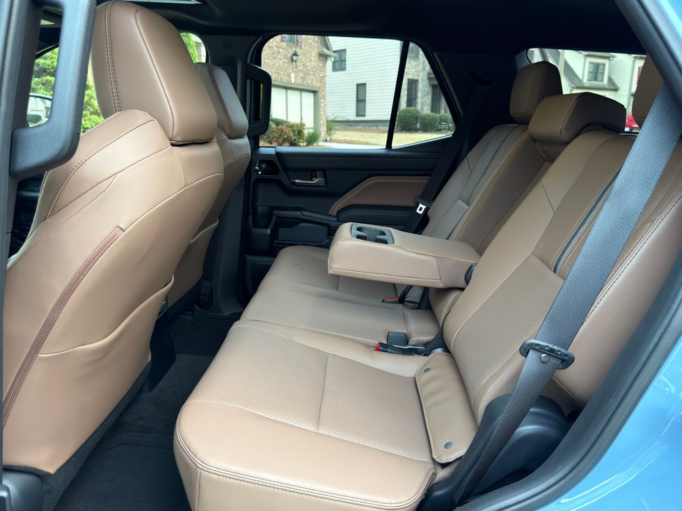 Tan leather vehicle rear seats with center armrest, cup holders, and seatbelts.