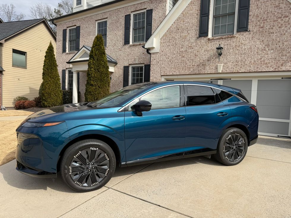 Teal SUV with distinctive black wheels parked on a concrete driveway in front of a brick house.