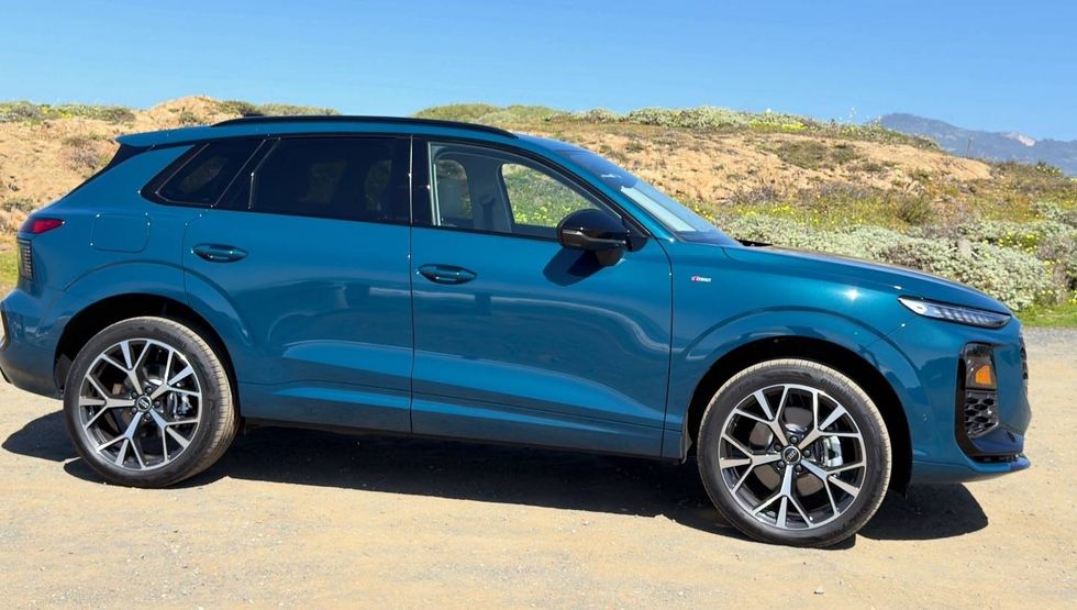 Teal VinFast SUV parked on a dirt road with hills and a blue sky in the background.