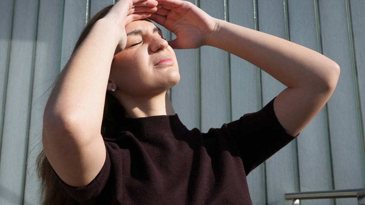 Teenage girl looking up at bright sun on sunny day. Young woman squinting and shielding her face with hands from sunlight. Ultraviolet exposure, skin protection, sun safety, UV radiation concept