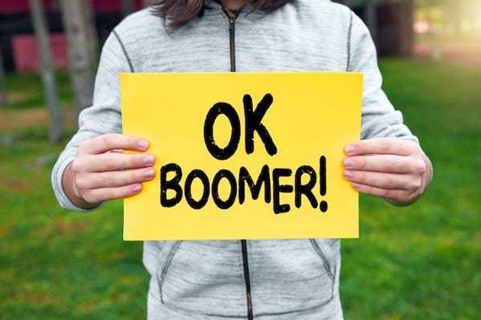 Teenager holds a banner with the words "Ok Boomer!" against nature background