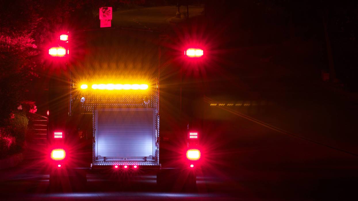 The back of a fire truck engine parked on the street with the lights on at night.