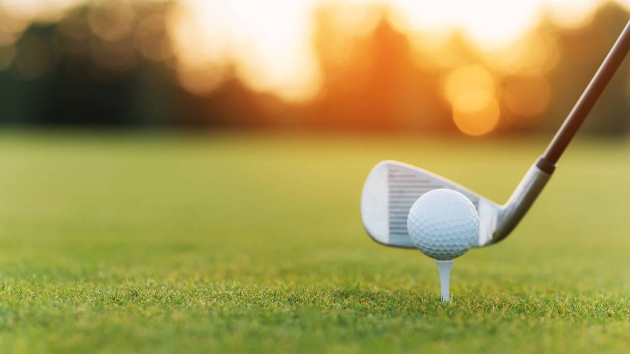 The golf club behind the golf ball on the stand