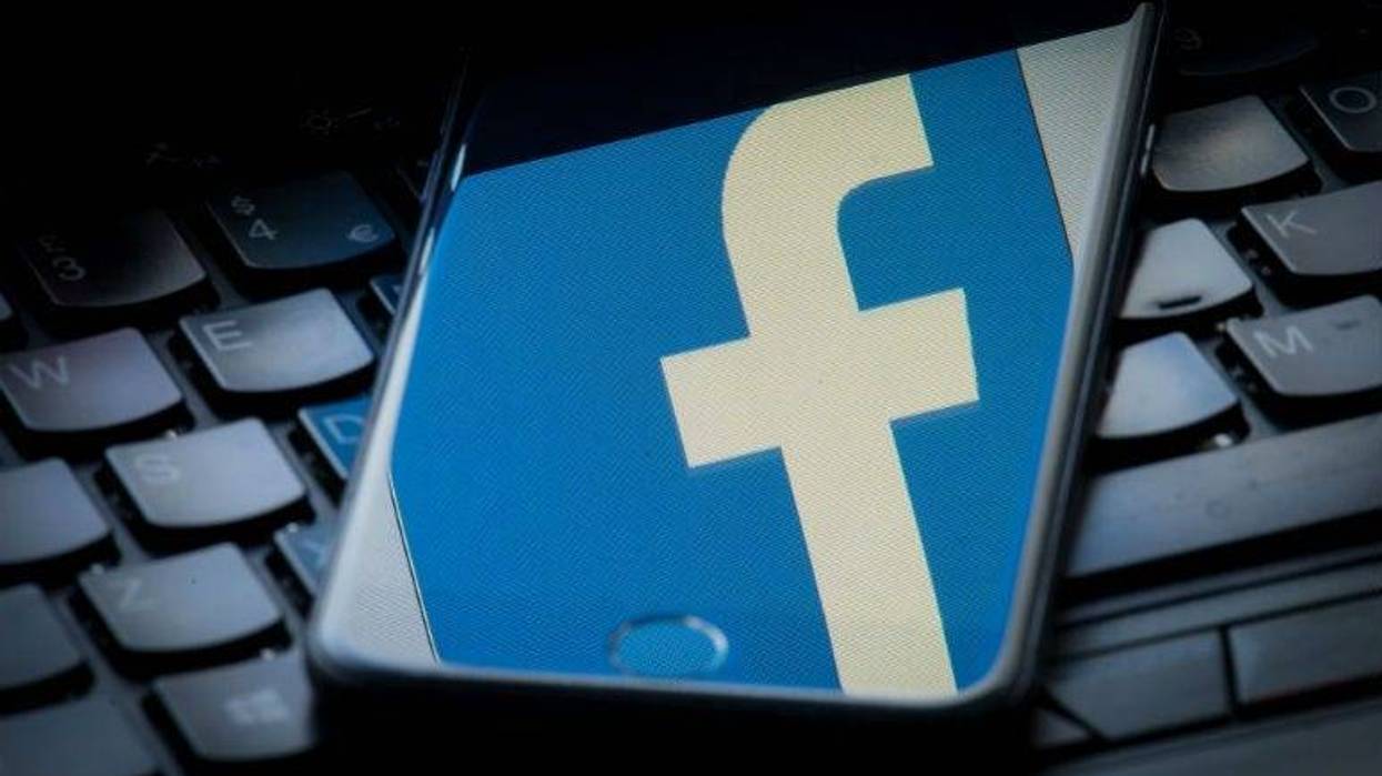 The logo of social networking site Facebook is reflected on the screen of a smartphone resting on a laptop keyboard.