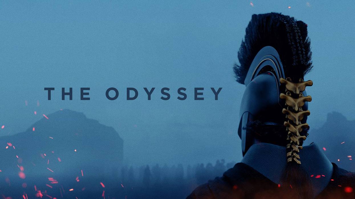 THE ODYSSEY title. Back of figure in dark helmet with golden spine, hazy mountains, and red sparks.