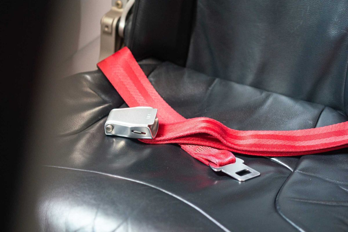 The safety seatbelt strap on the empty airplane passenger seat, safety equipment object for the transportation. Close-up and selective focus.