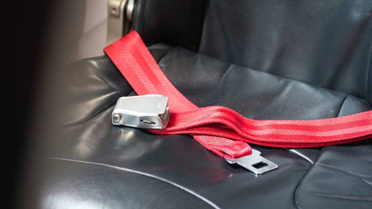 The safety seatbelt strap on the empty airplane passenger seat, safety equipment object for the transportation. Close-up and selective focus.