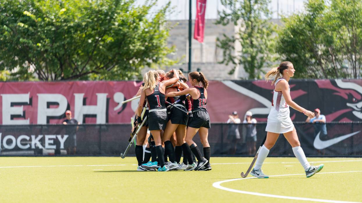 The Saint Joseph’s University field hockey team celebrates on the field.