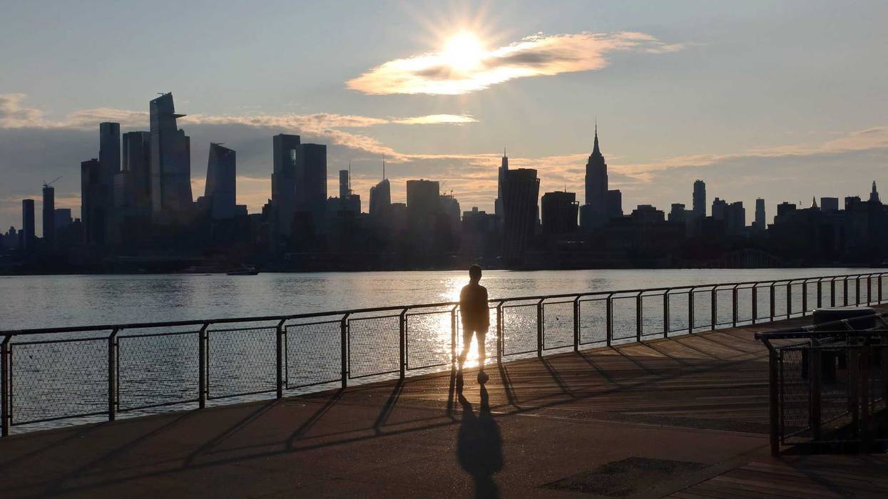 The sun rises behind the skyline of Midtown Manhattan as a person walks on a pier by the Hudson River on June 9, 2023, in Hoboken, New Jersey