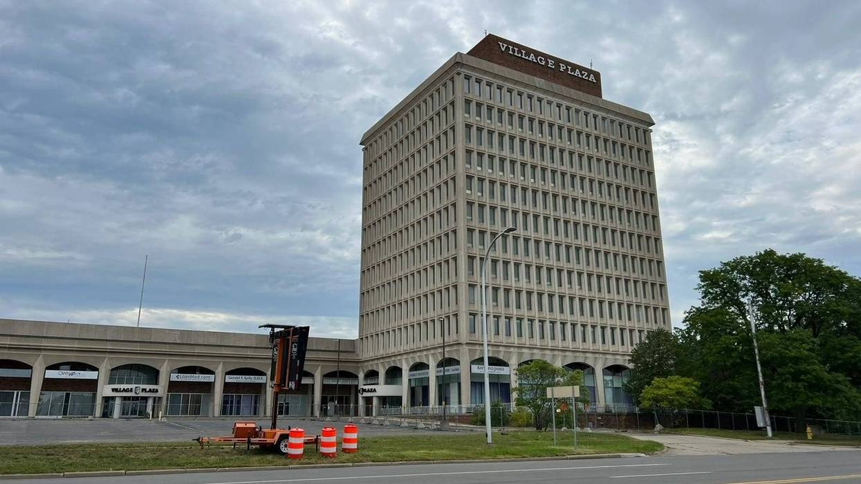 The vacant 12-story Village Plaza building. The lot is empty with the freeway running behind it.