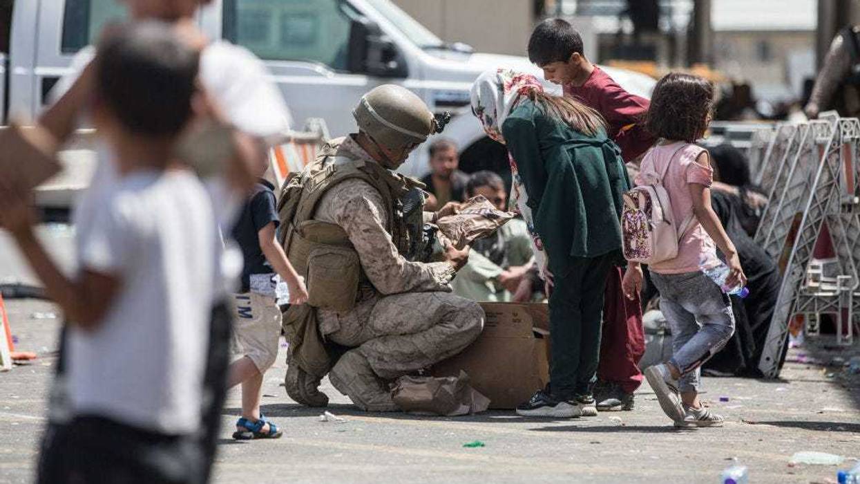 This handout image shows A Marine with Special Purpose Marine Air-Ground Task Force-Crisis Response-Central Command (SPMAGTF-CR-CC) provides meals ready-to-eat to a child during an evacuation at Hamid Karzai International Airport, August 20, 2021 in Kabul, Afghanistan. U.S. service members are assisting the Department of State with an orderly drawdown of designated personnel in Afghanistan. (Photo by Sgt. Samuel Ruiz / U.S. Marine Corps via Getty Images)