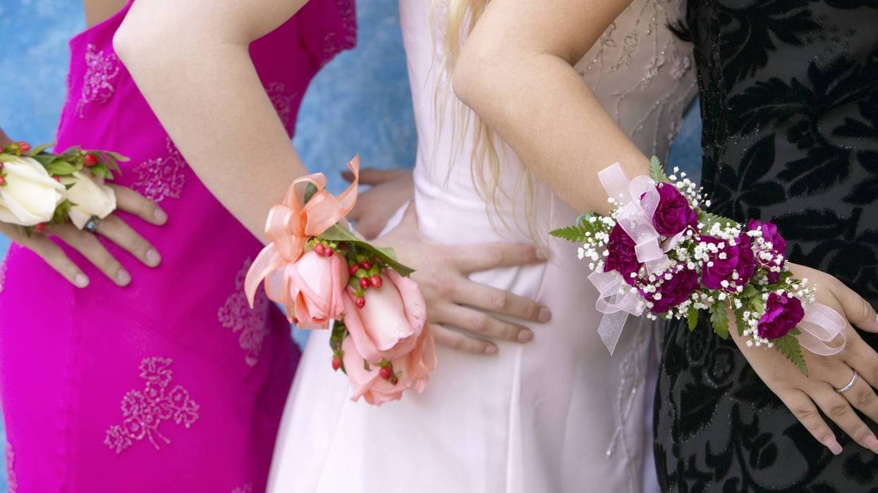 Three girls in formal dresses with wrist corsages, hands on each other's backs.