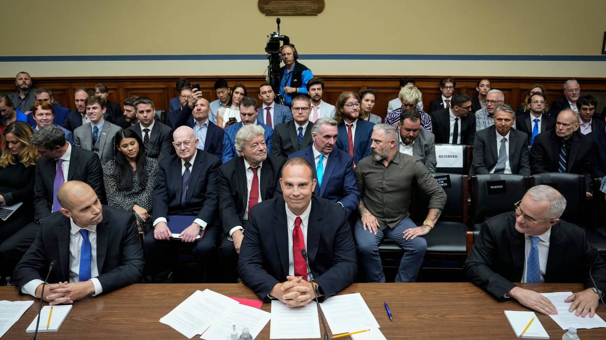 three men sit at panel in house committee room with a crowd in the seats behind them