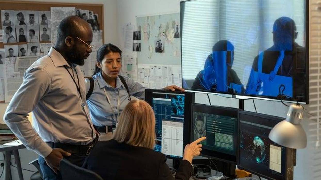 Three police officials huddle around four computer monitors