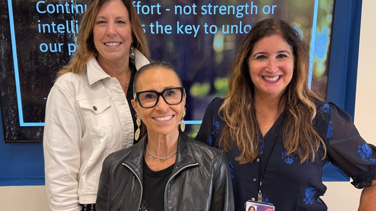 Three smiling professional women stand in front of a screen with a motivational quote.