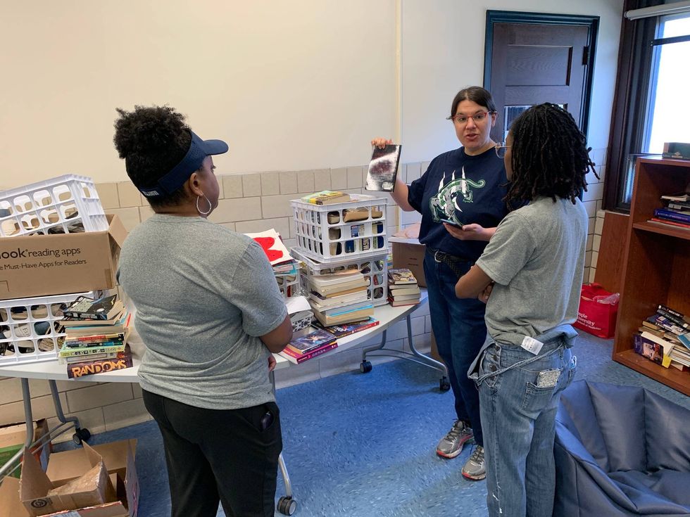 Three women standing in a room with crates of books.