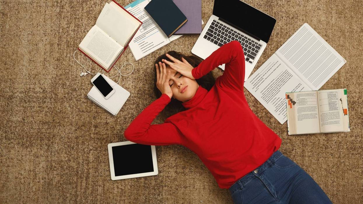 Tired student girl lying on the floor with books and gadgets
