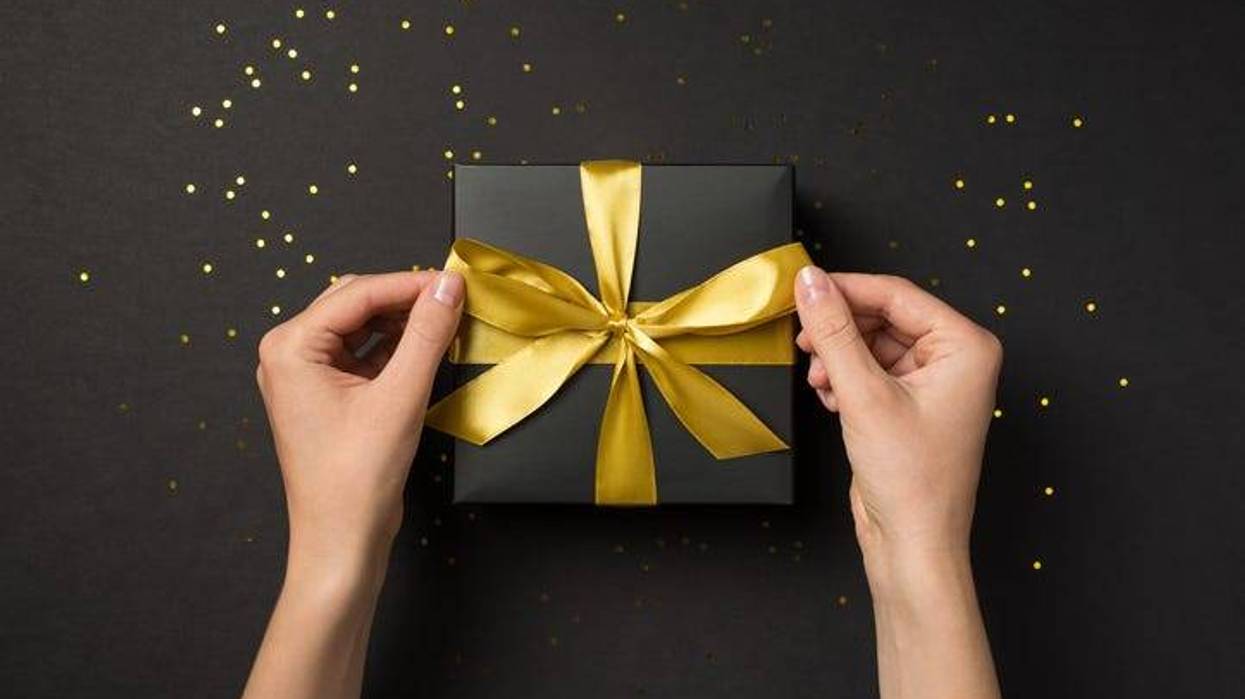 top view photo of female hands tying golden ribbon bow on black giftbox over golden sequins on isolated black background