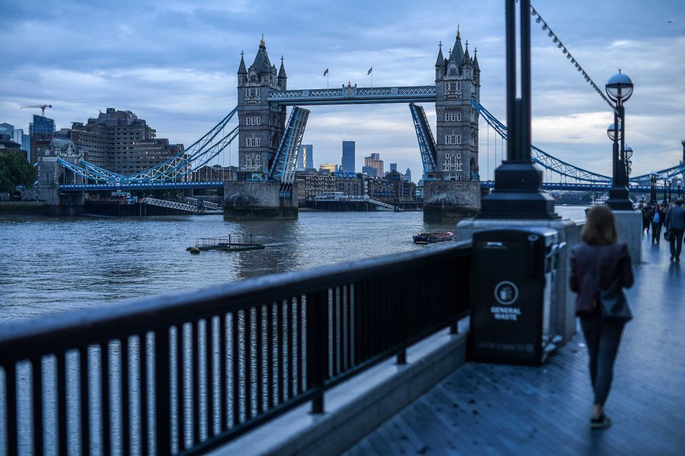 Tower Bridge is seen stuck in the raised position as people walk along the south bank.
