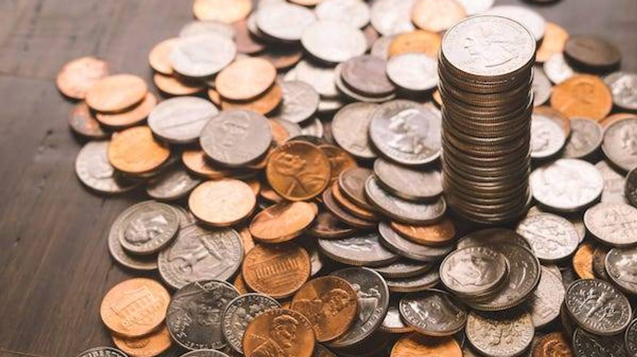 Tower of quarters with money spread of bamboo wood background and includes quarters, nickels, dimes, and pennies.