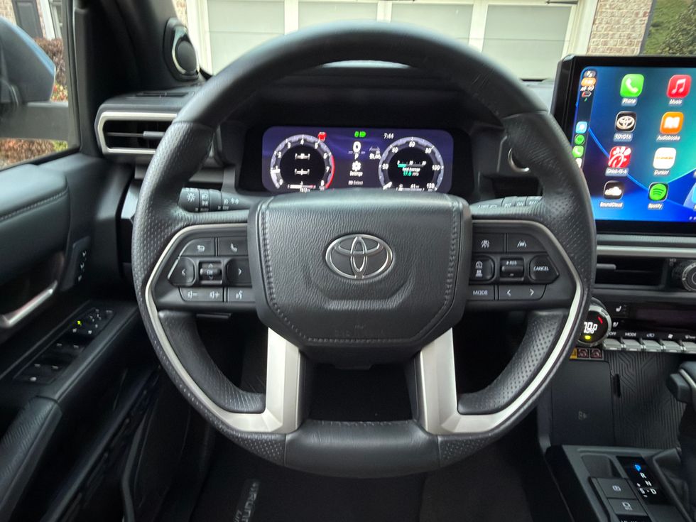 Toyota car interior: steering wheel, digital gauges, and large Apple CarPlay infotainment screen.