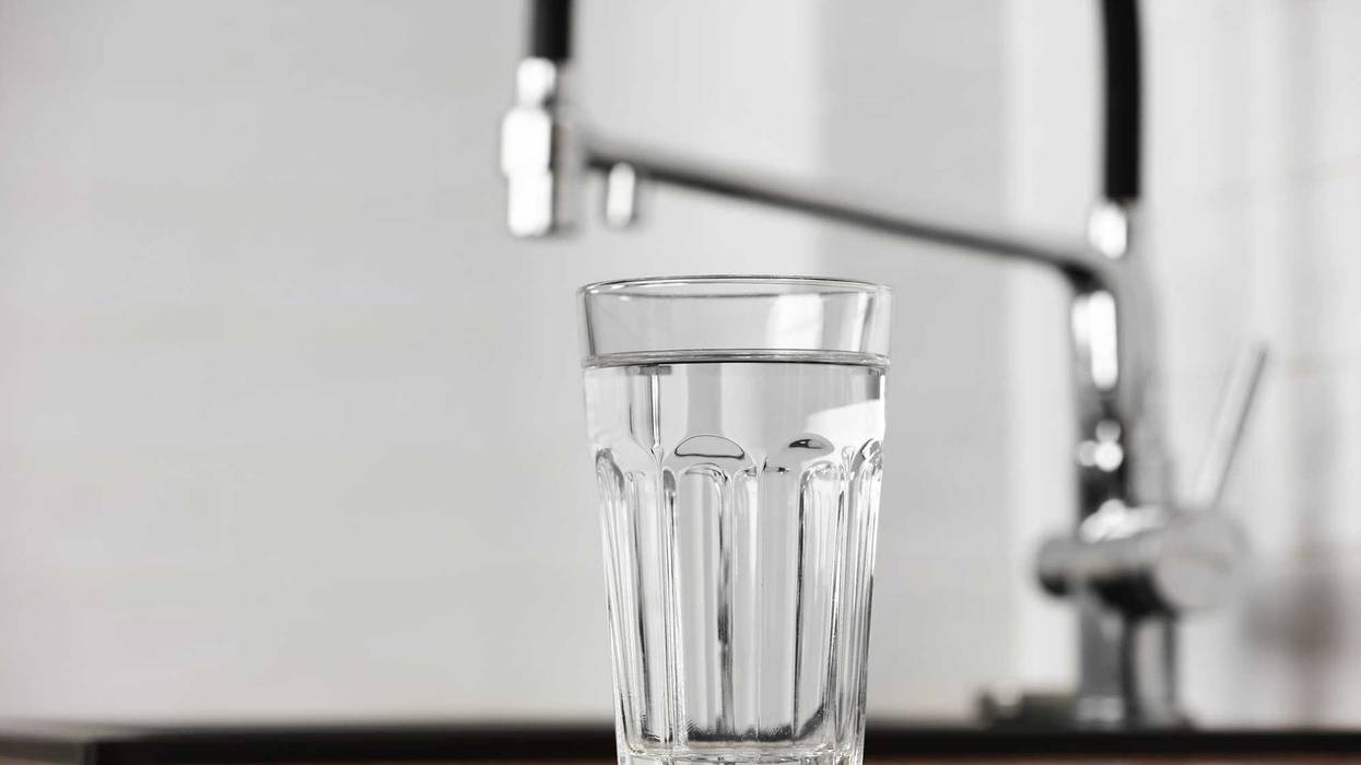 Transparent glass of clean filtering water on wooden table in kitchen interior. Tap with purified water with an osmosis system of the home kitchen sink.