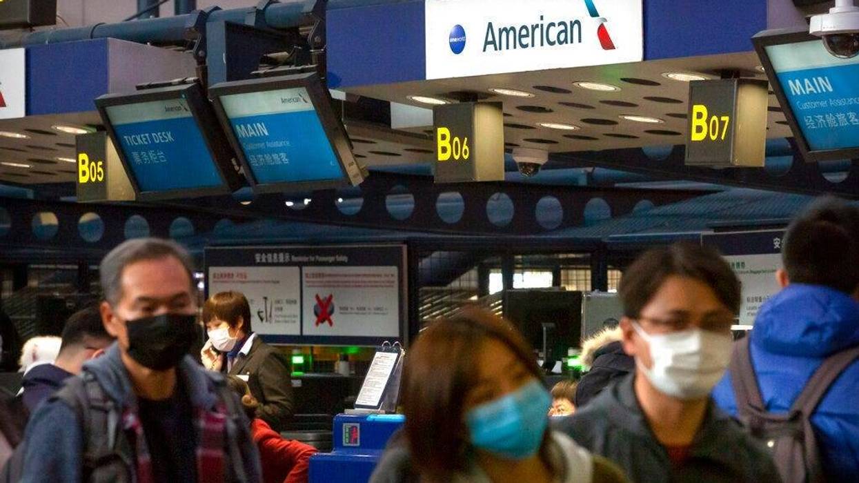 Travelers wearing face masks line up to check in for an American Airlines flight to Los Angeles at Beijing Capital International Airport in Beijing,