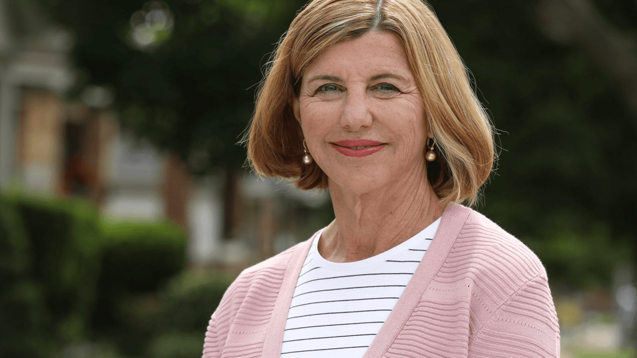 Trudy Busch Valentine stands outside smiling. she is a white woman with short strawberry blond hair, a black and white striped t shirt and a light pink cardigan