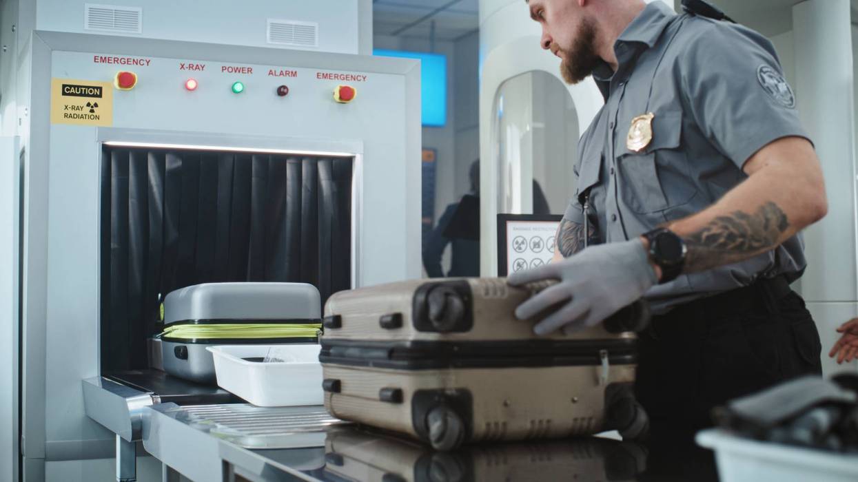 TSA Worker Putting Luggage and Personal Items in Trays on Conveyor Belt with X-ray Metal Detector