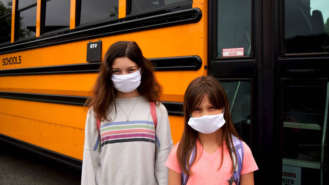 Two children wearing face masks by school bus - stock photo