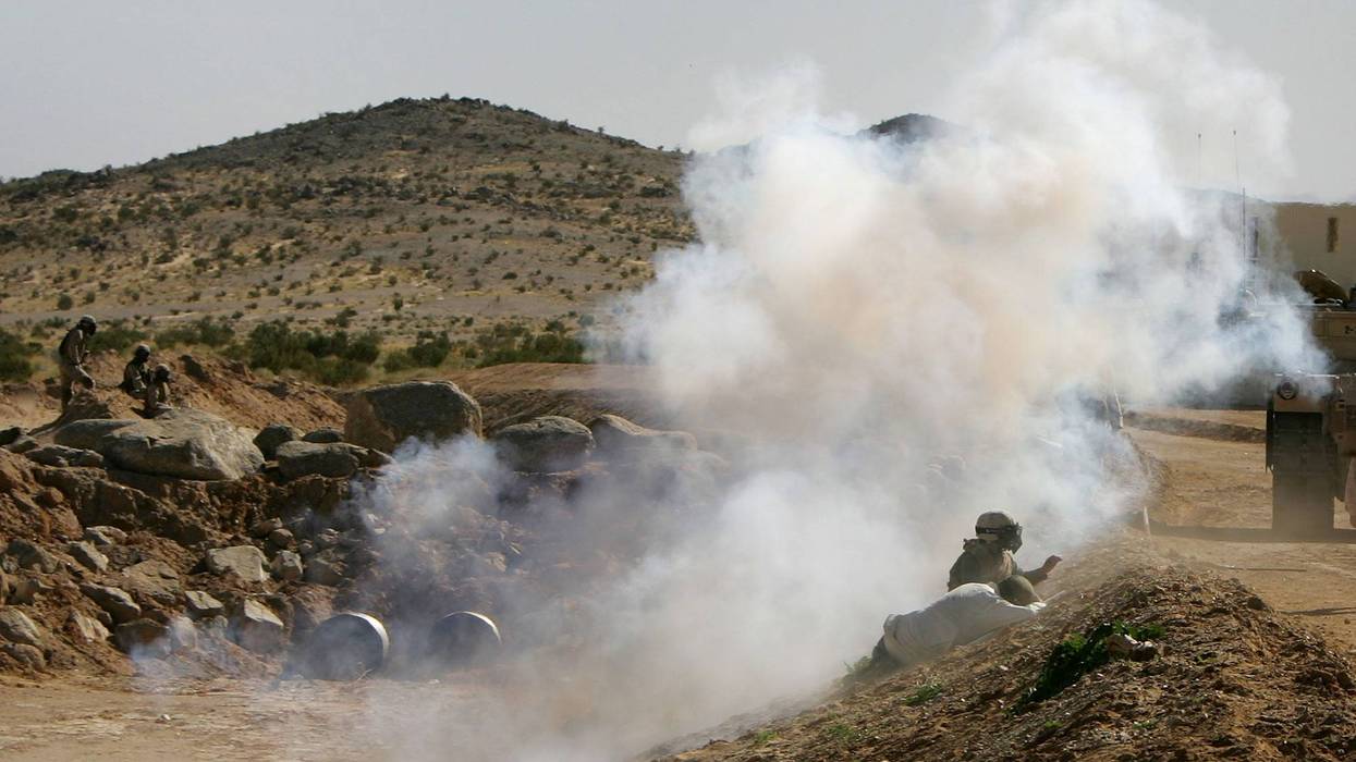 Two civilian Iraqi role players are seen as smoke from a mock IED (Improvised Explosive Device), or roadside bomb, envelops U.S. Marines on a practice urban assault at Range 215 simulated Iraqi village at the Twentynine Palms Marine Base on November 15, 2005 near Twentynine Palms, California. The marines have turned shipping containers into simulated Iraqi villages on Ranges 200 and 215 to train their fighters in an urban environment similar to that which they will be deployed to in Iraq. The Marines will be conducting Stability and Support Operations next year in Iraq with emphasis on training and mentoring Iraqi Security Forces. (Photo by David McNew/Getty Images)