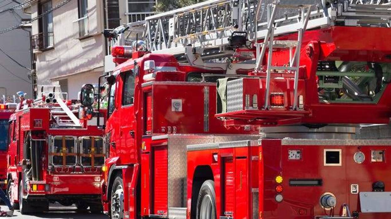 Two fire trucks lined up along the side of a house