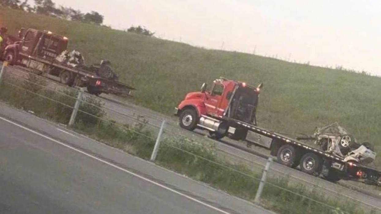 Two flatbed tow trucks on a grassy roadside, each carrying a heavily damaged car.