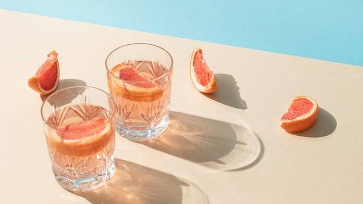 Two glasses of drink with slices of fresh grapefruit against bright beige and blue background