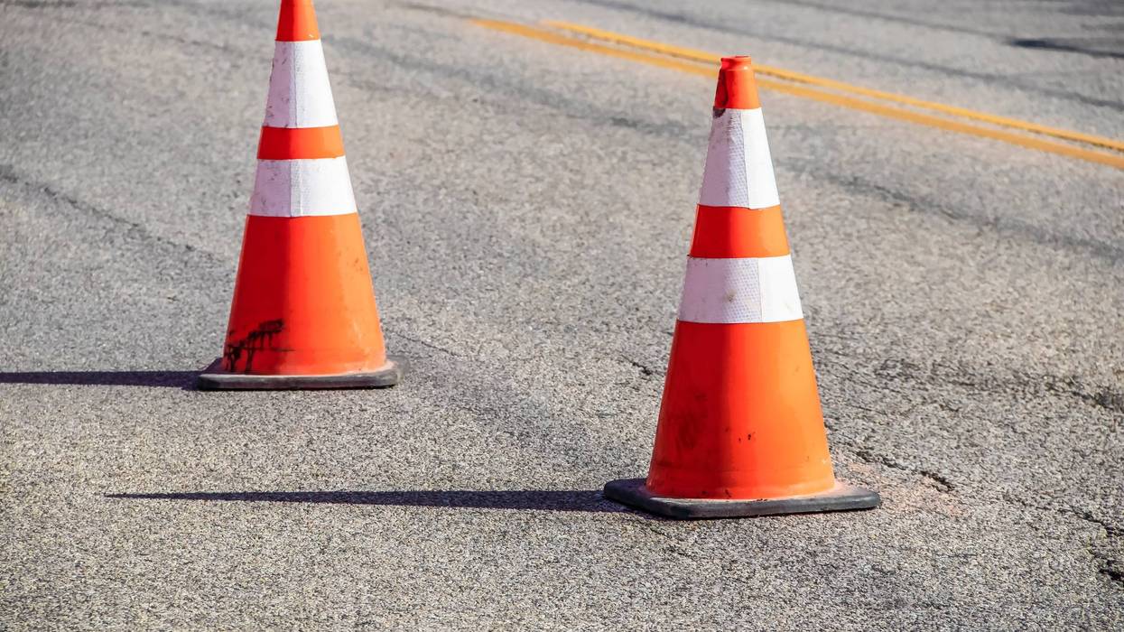 Two grungy orange traffic cones with reflective tape and sharp shadows on cracked asphalt pavement