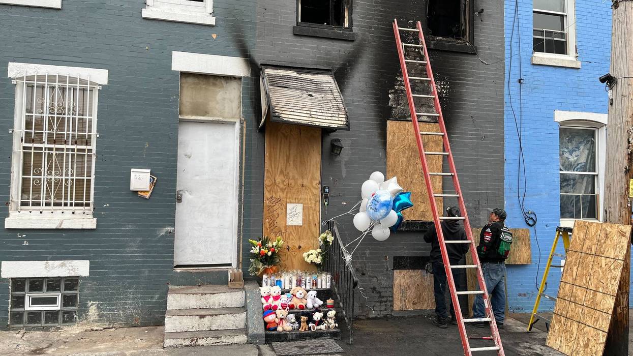 Two men board up the row house that caught fire on April 24, 2022, killing a father and his three children inside. The mother jumped out a second-story window and survived.
