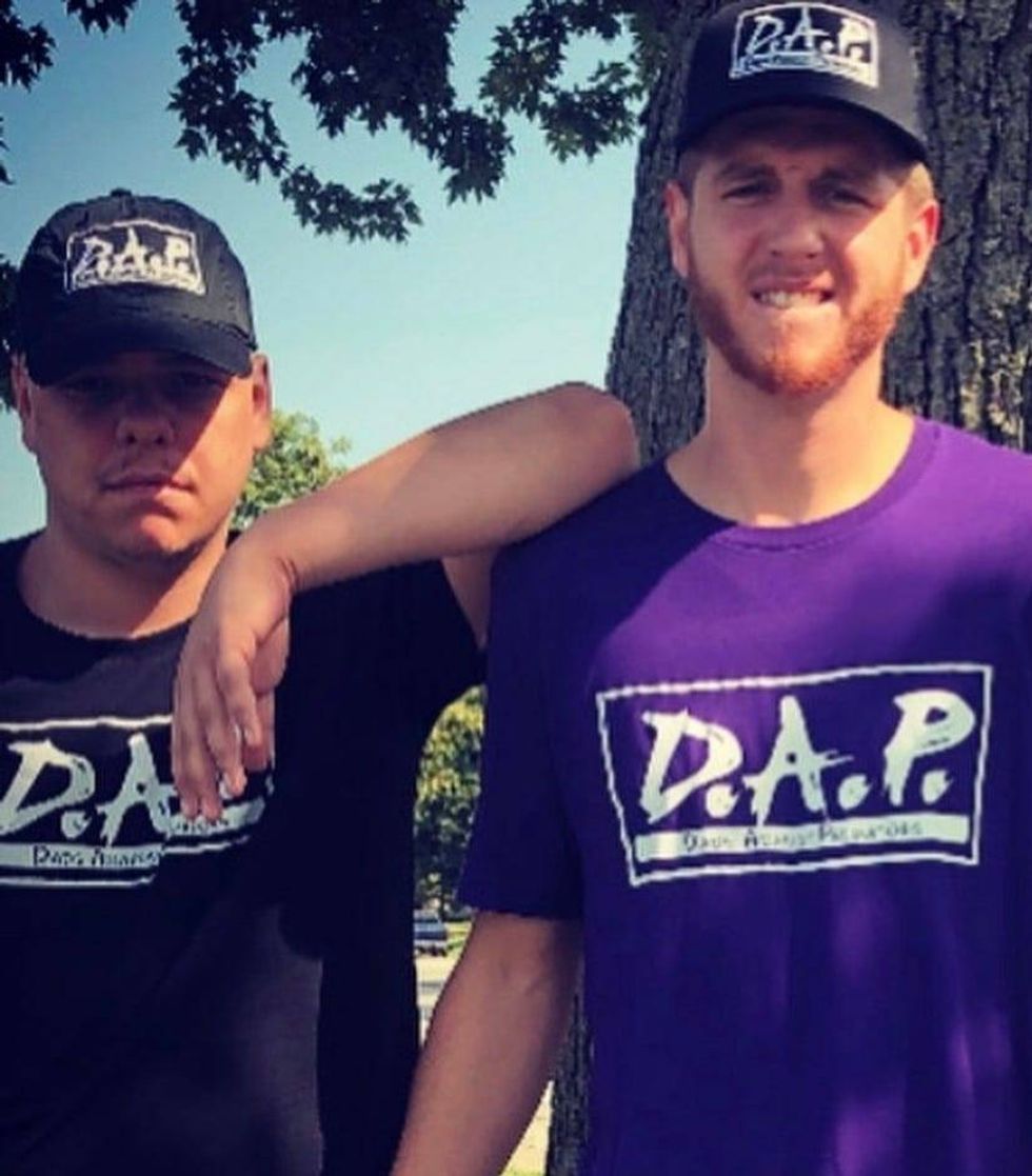 Two men standing side-by-side wearing D.A.P t-shirts