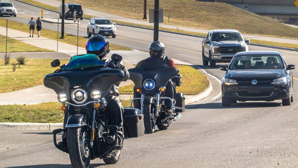 Two motorcyclists navigate a winding road, enjoying a scenic ride with a backdrop of autumn foliage.