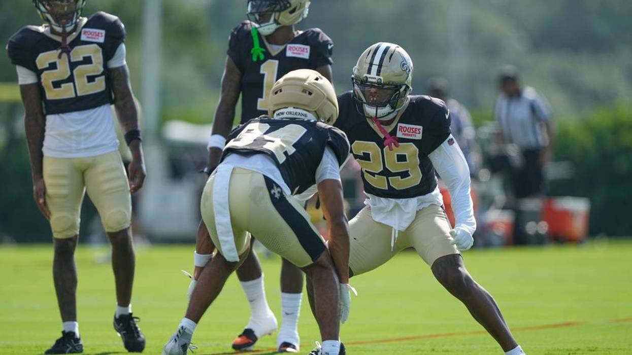 Two New Orleans Saints players in black and gold are crouched, facing off at practice.