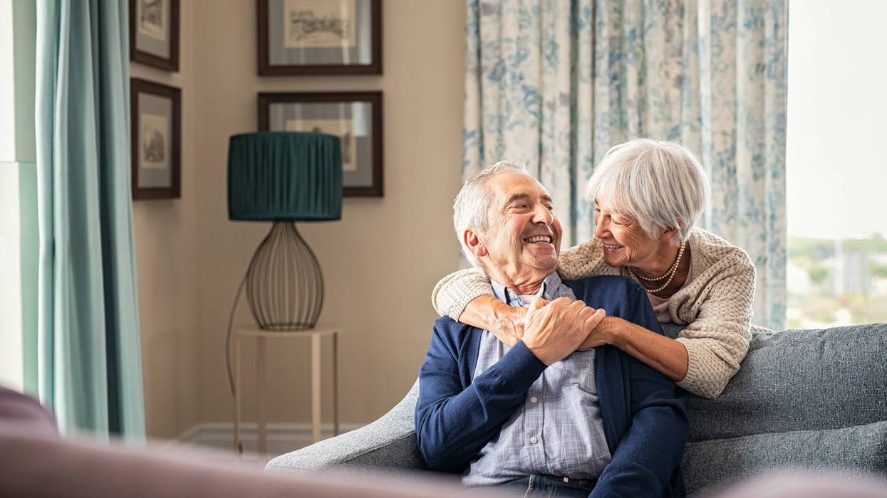 two old people sittng on couch holdinghands and smiling