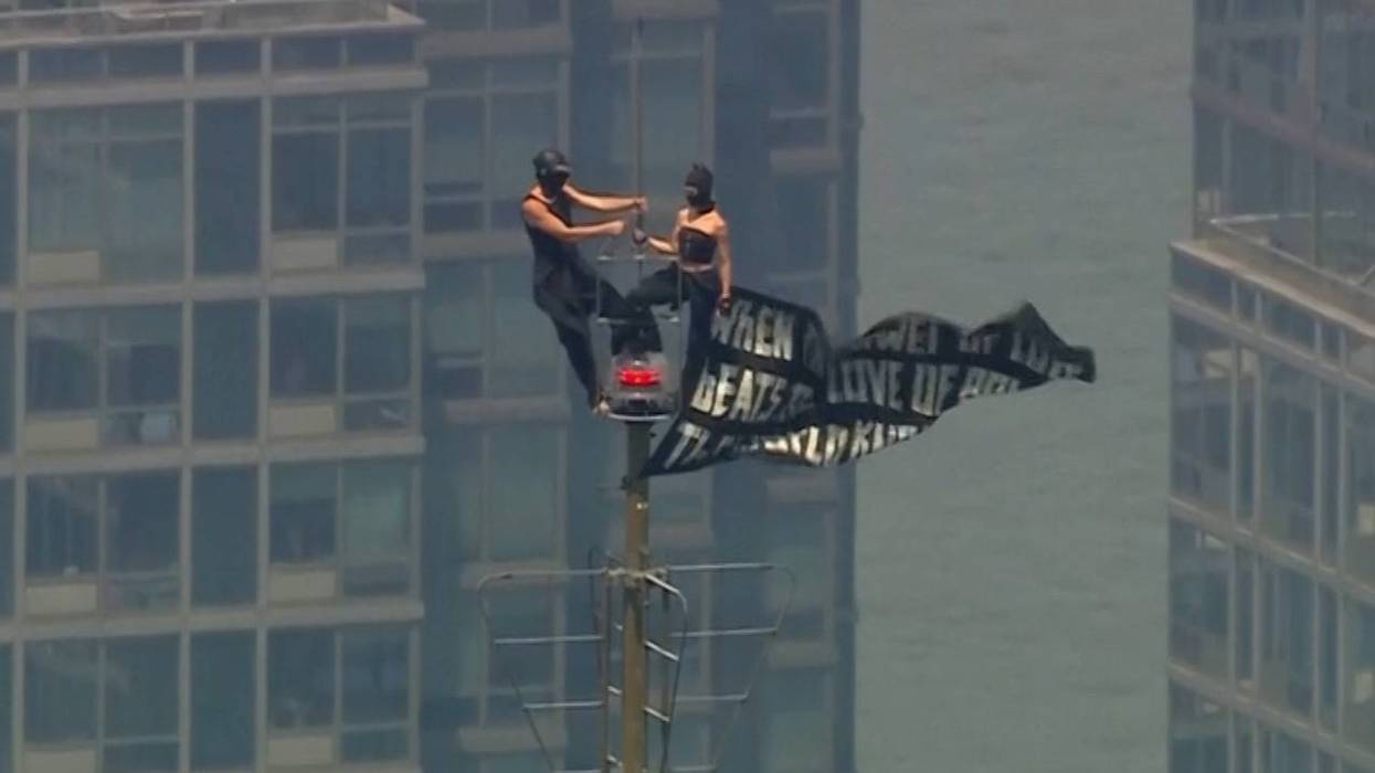 Two people stand on the tip of the antenna of the Empire State Building while holding a banner on Wednesday, July 1.