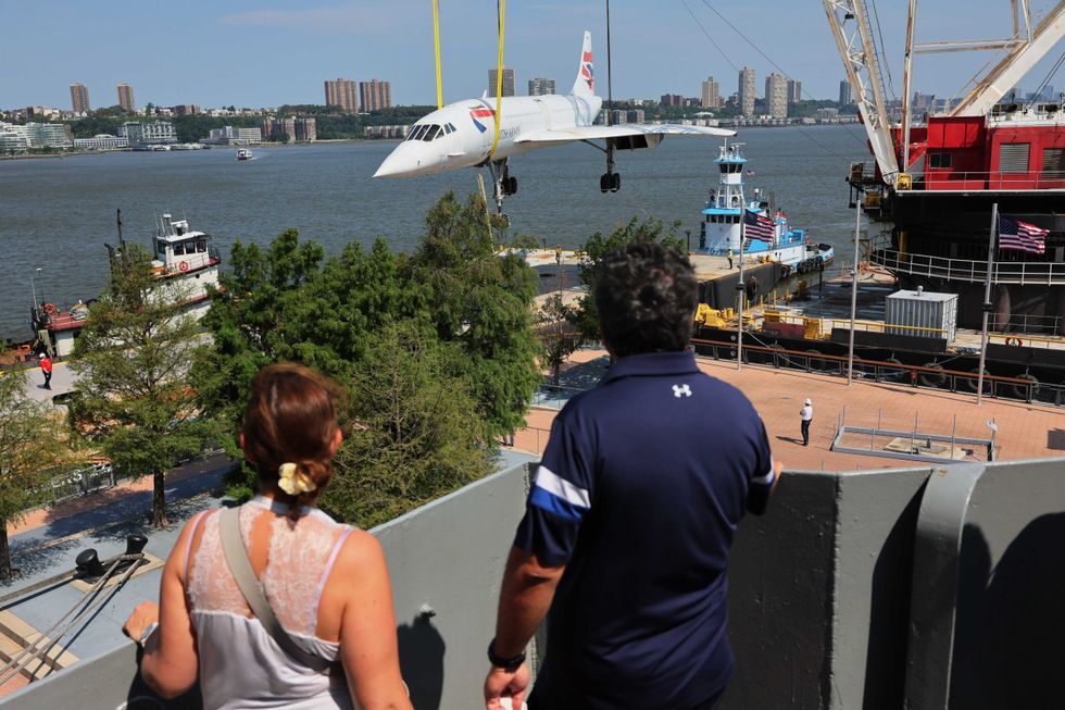 Two people watch as the Concorde is hoisted into the sky.