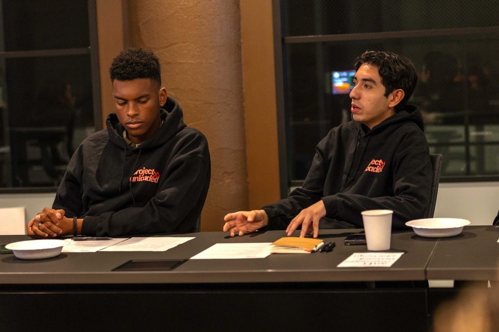 Two Project Unloaded male students sit at table discussing.